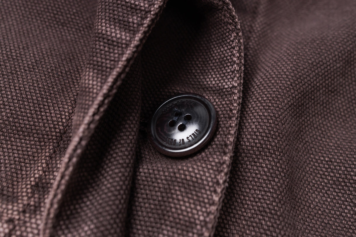 Close-up of a dark brown textured fabric garment with a black button on the collar placket.