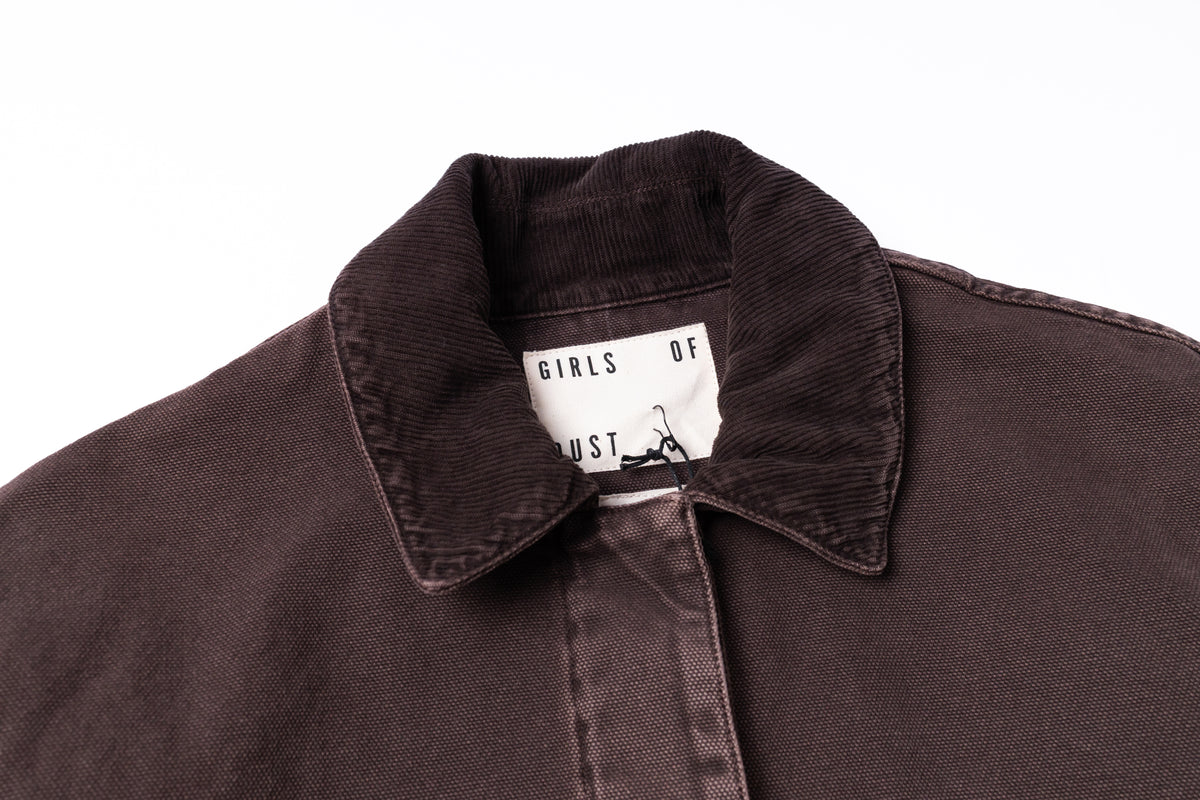 Close-up of a dark brown corduroy jacket collar with a white inner neck label reading 'GIRLS OF JUSTICE'.