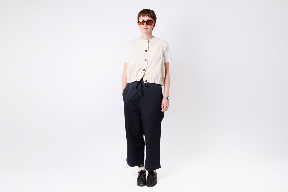 Person wearing a cream shirt and dark pants on a white background