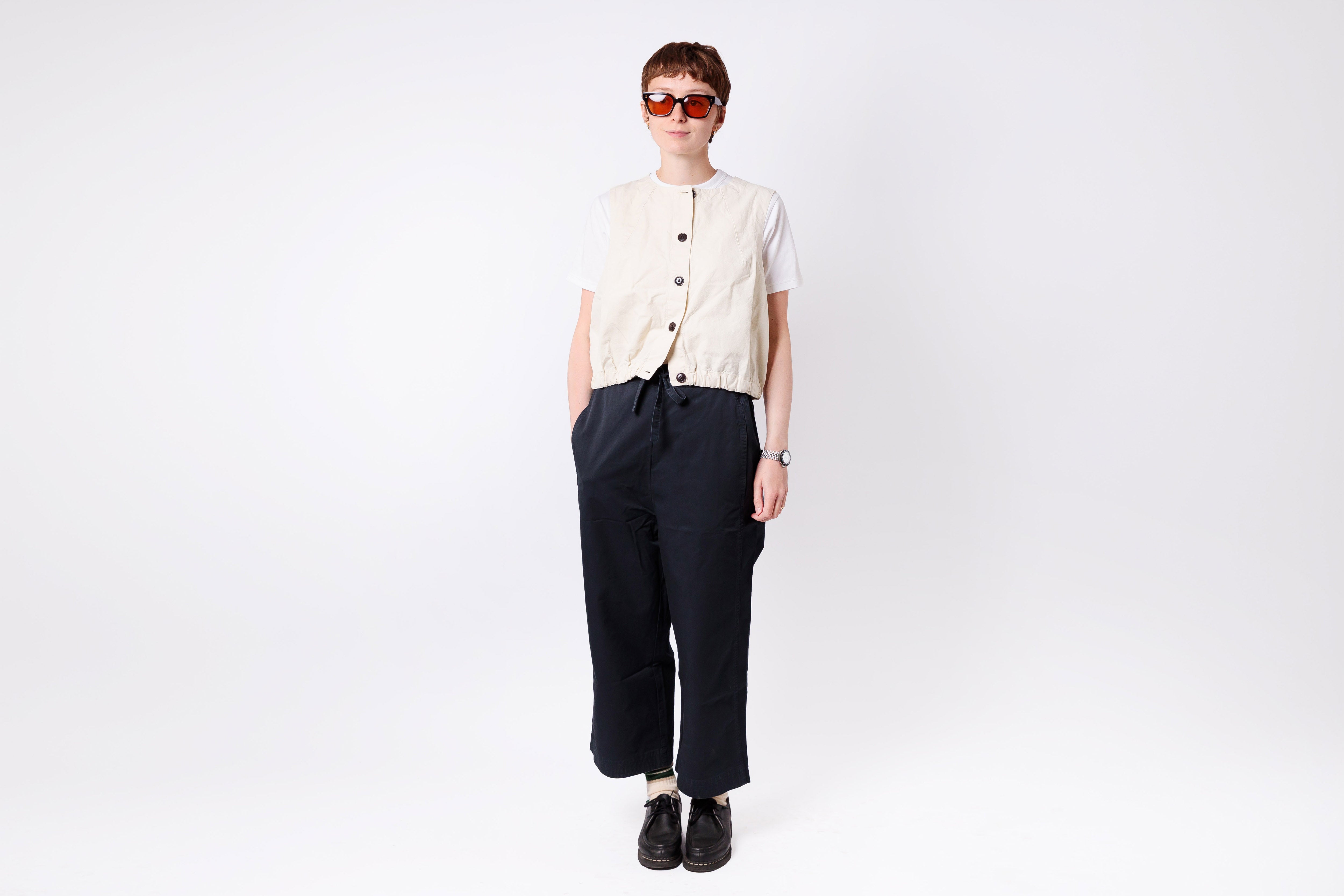 Person wearing a cream shirt and dark pants on a white background