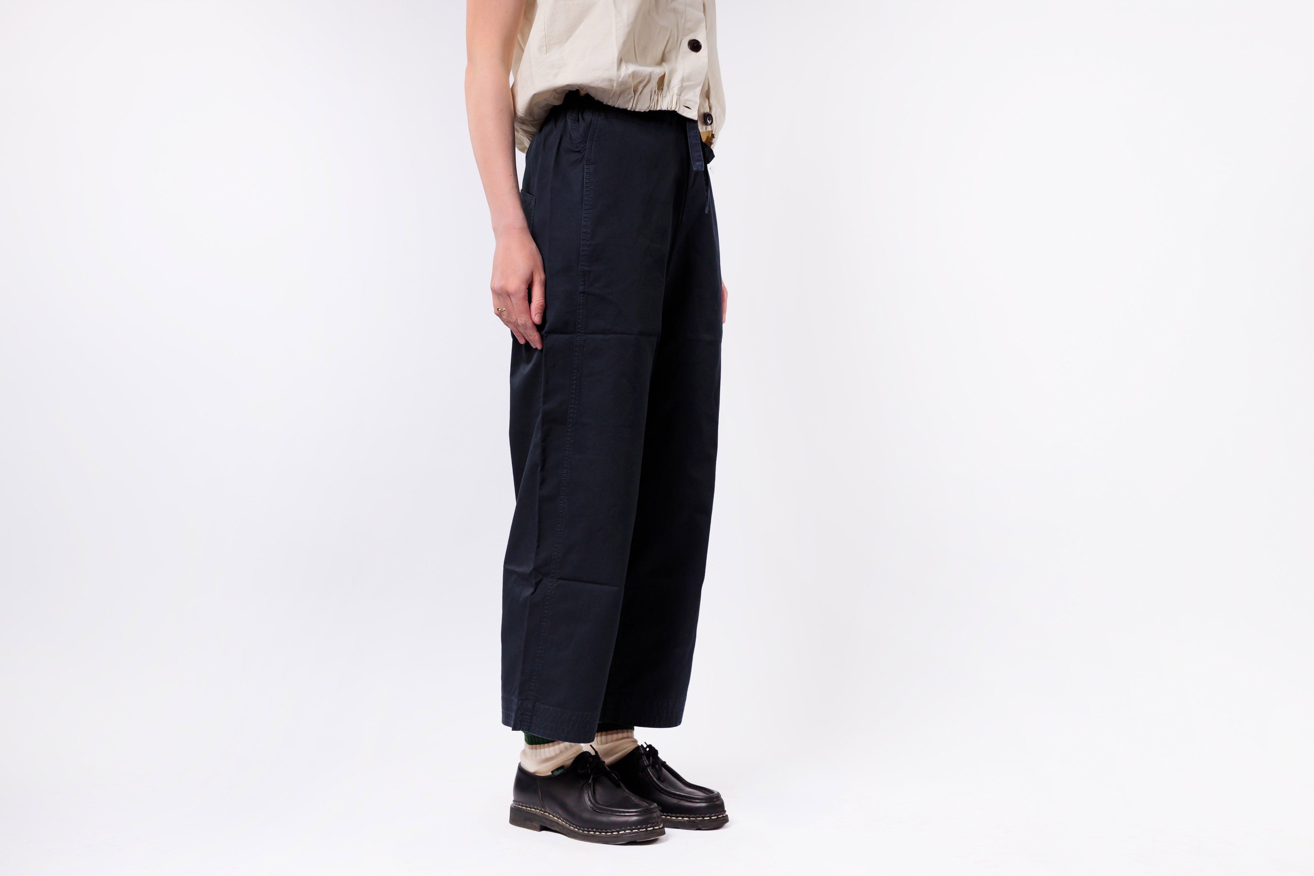 Person wearing dark pants and black shoes on a white background
