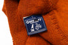 Close-up of an orange sweater with a Guernsey Woollens label on a white background