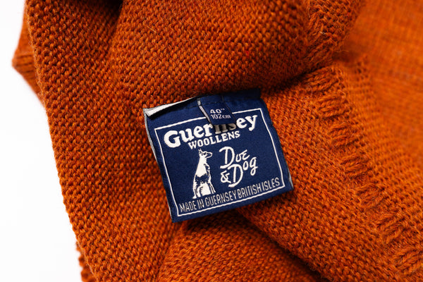 Close-up of an orange sweater with a Guernsey Woollens label on a white background