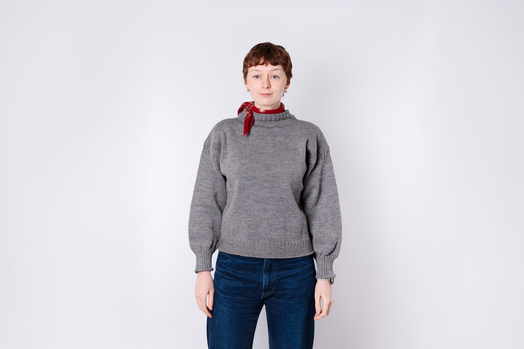 Person wearing a gray sweater and blue jeans with a red bandana on a white background