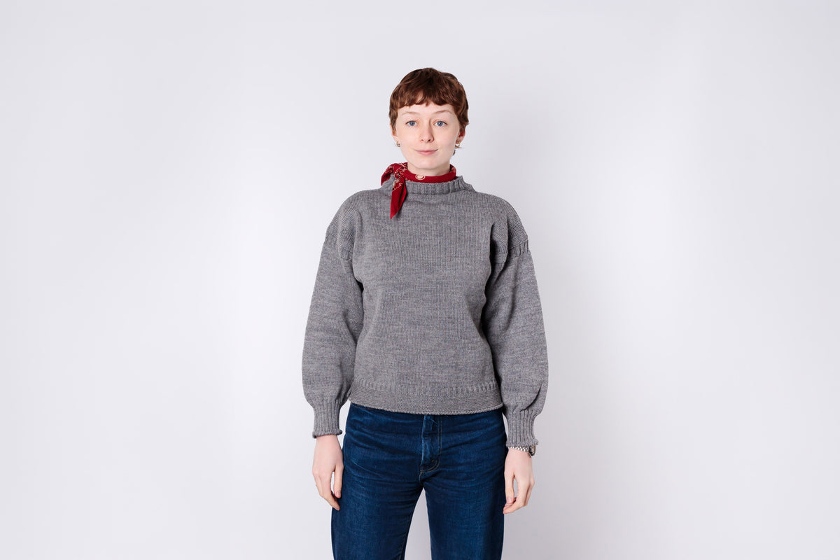 Person wearing a gray sweater and blue jeans with a red bandana on a white background