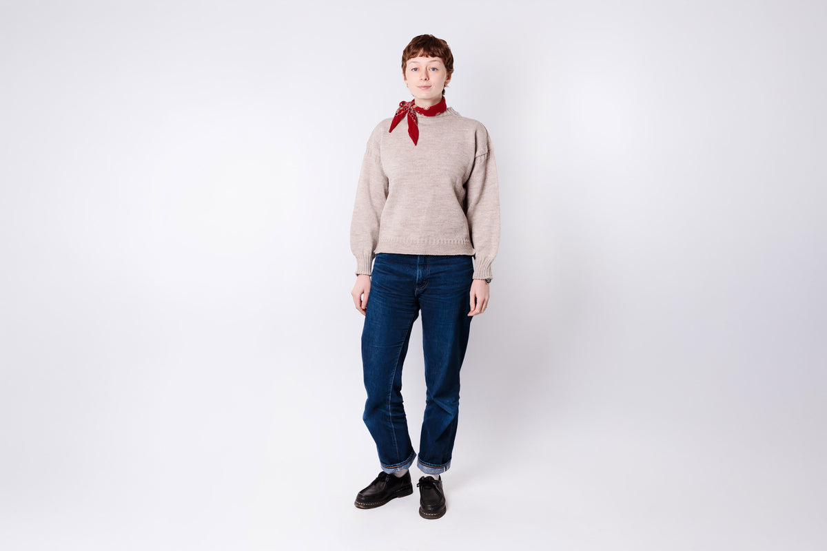 Person wearing a beige sweater, blue jeans, and a red scarf on a white background
