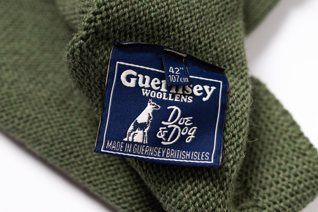 Close-up of a Guernsey Woollens label on a green knitted fabric.