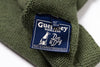 Close-up of a Guernsey Woollens label on a green knitted fabric.