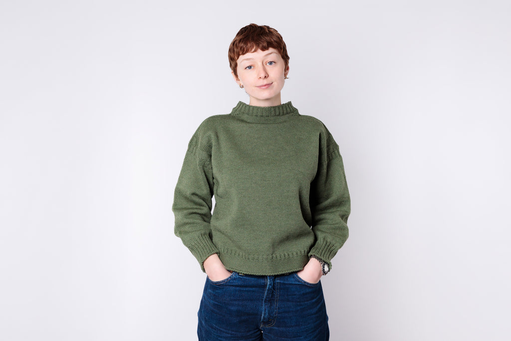 Person wearing a green sweater and blue jeans against a white background