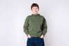 Person wearing a green sweater and blue jeans against a white background