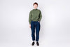 Person wearing a green sweater and blue jeans on a white background