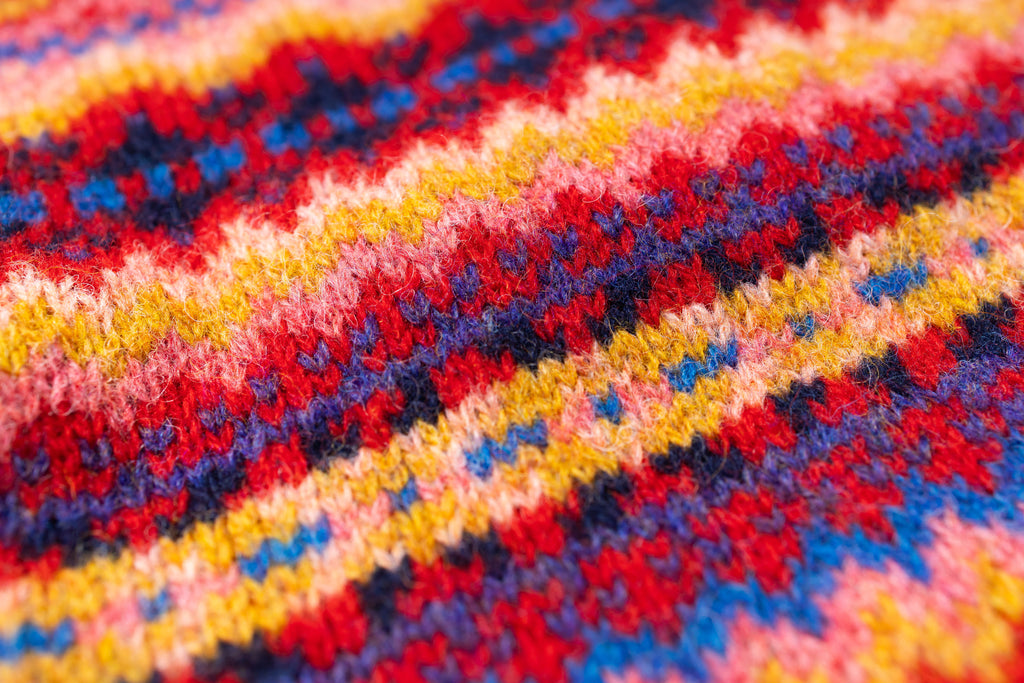 Close-up of a colorful knitted fabric with red, yellow, blue, and pink patterns.