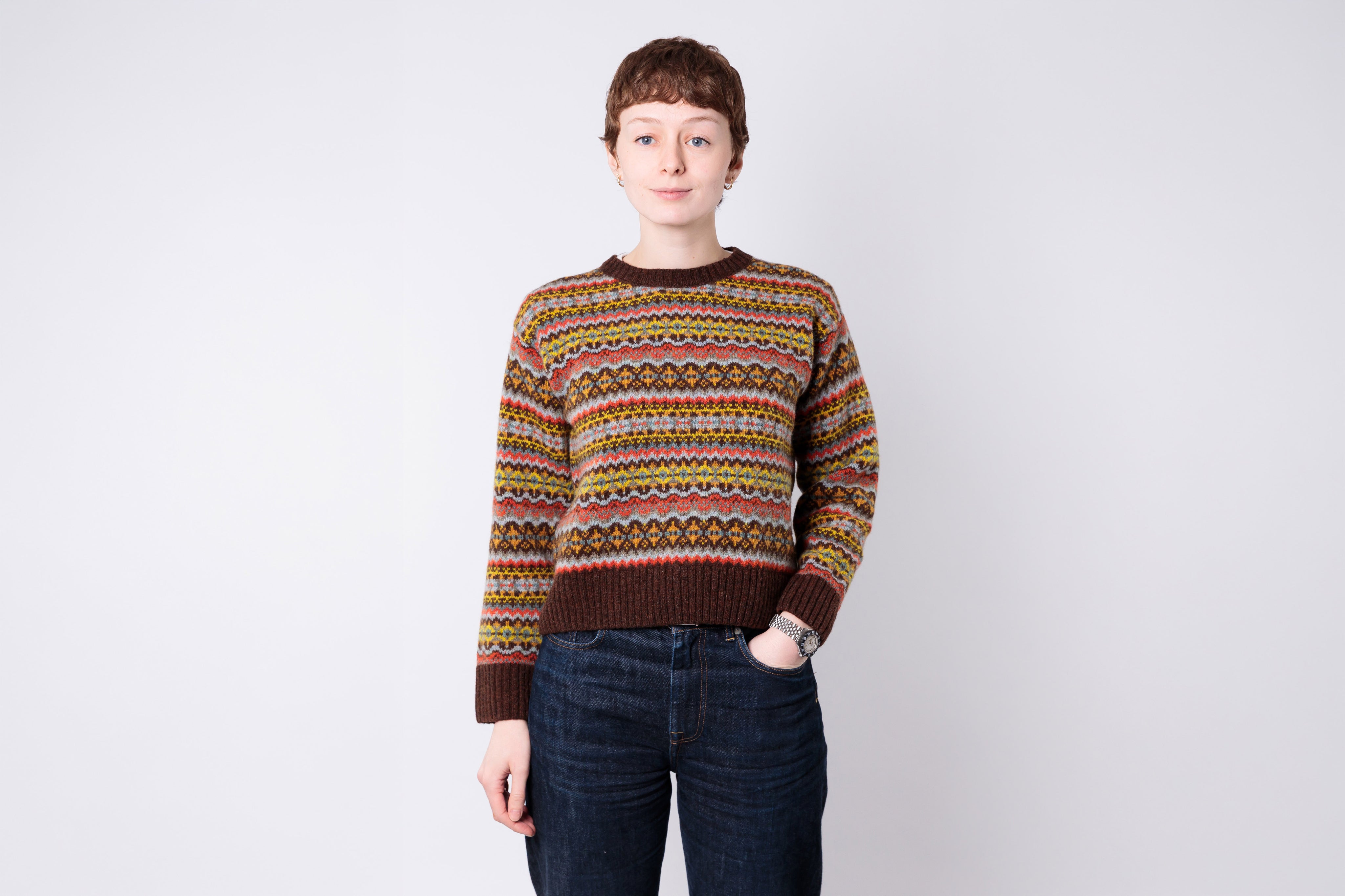 Person wearing a patterned sweater and jeans on a plain background
