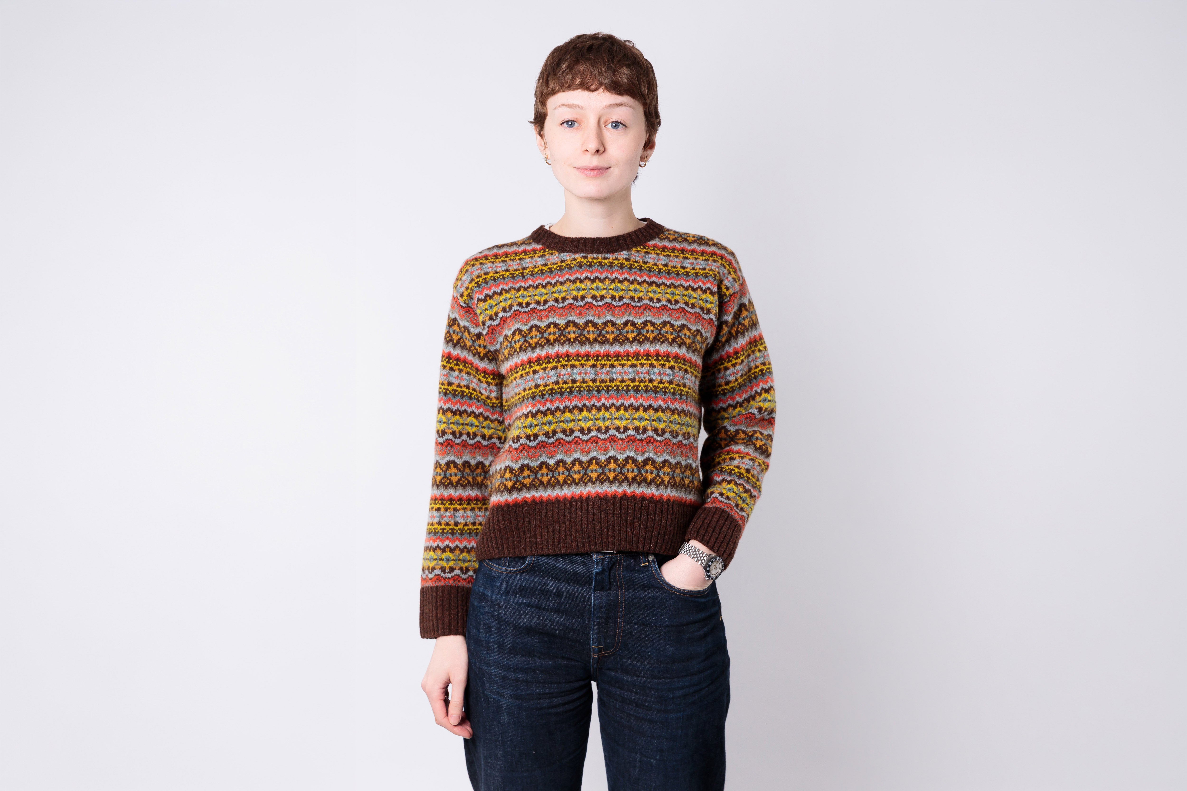 Person wearing a patterned sweater and jeans on a plain background