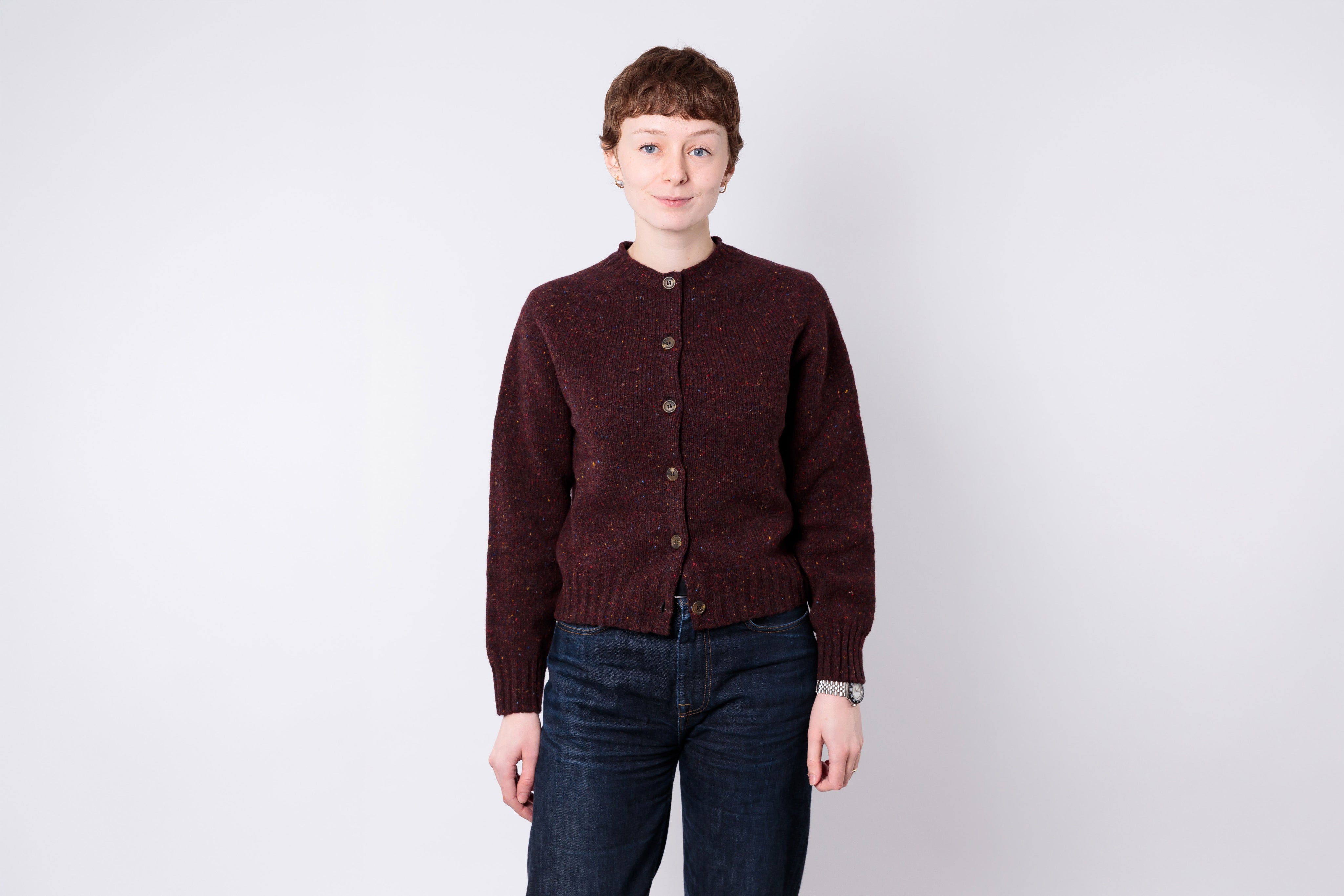 Person wearing a maroon cardigan and dark jeans on a white background