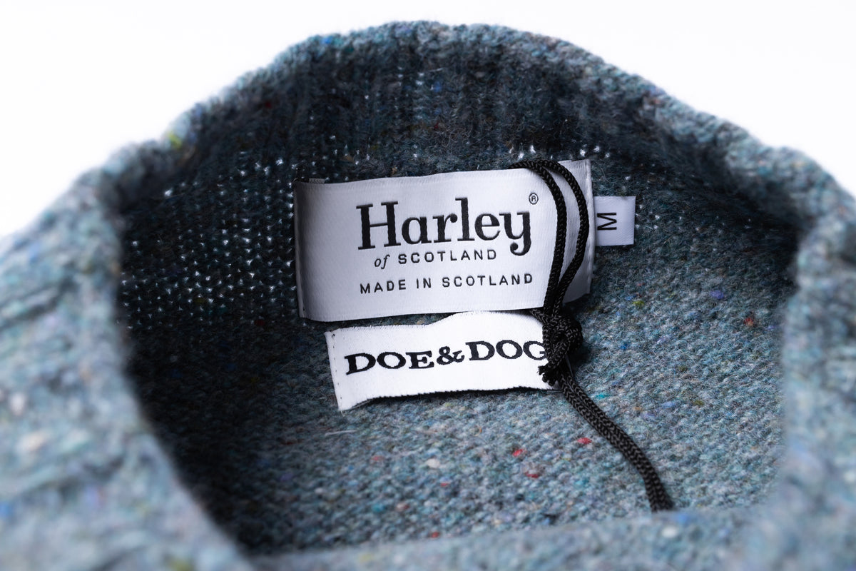 Close-up of the inside collar of a blue-gray knit sweater showing two brand labels: Harley of Scotland and Doe & Dog, with a size tag reading M.