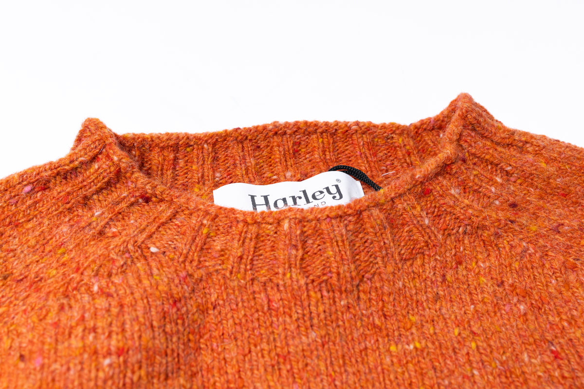 Close-up of a ribbed knit sweater neck in a heathered burnt orange color, featuring a white fabric tag with the brand name 'Harley'.
