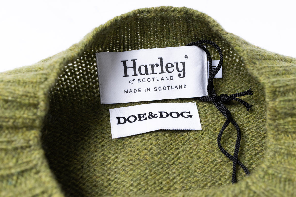 Close-up of the inside collar of a green knit sweater showing two brand labels: Harley of Scotland and DOE&DOG, with a black drawstring cord.
