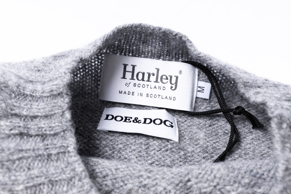 Close-up of the inside neckline of a gray knit sweater, showing two brand labels: Harley of Scotland and DOE&DOG, with a black drawcord cord.