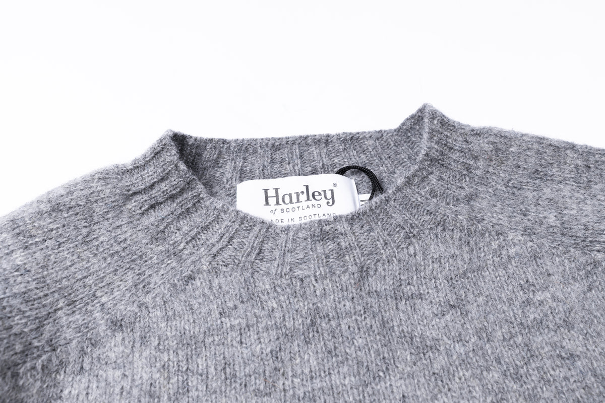 Close-up of a gray knit sweater with a white Harley label at the collar, shown against a plain white background.