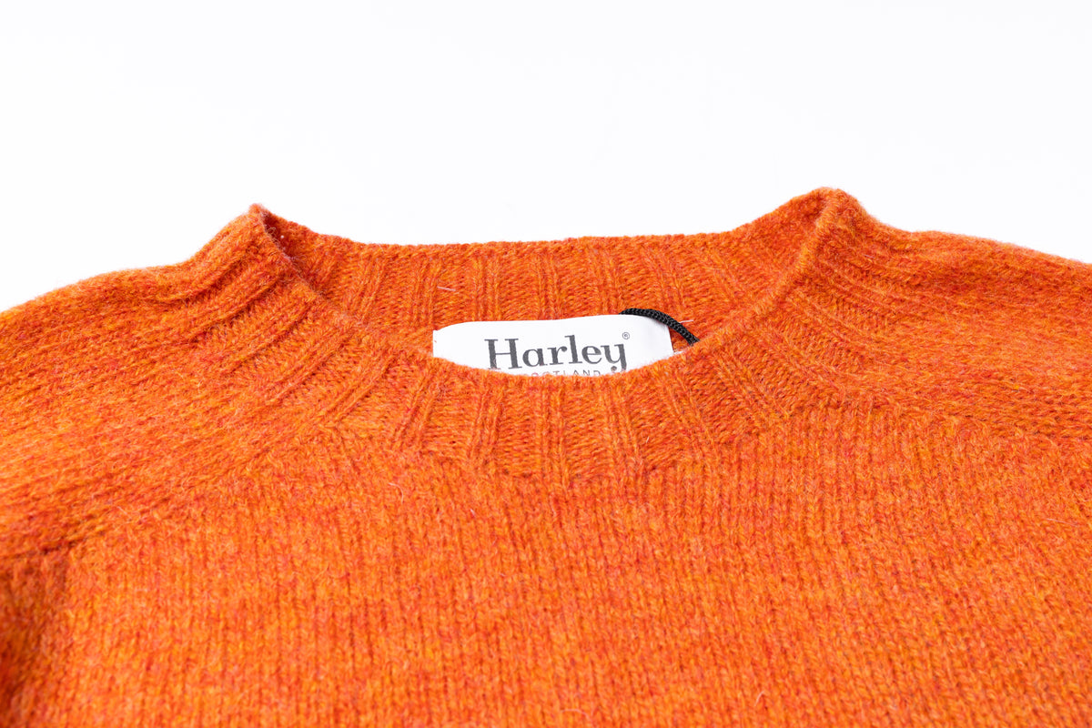 Close-up of a textured orange knit sweater with a white Harley-Davidson neck label visible inside the collar, set against a plain white background.