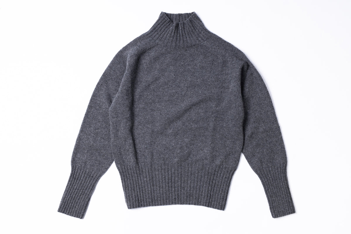 A dark gray knit turtleneck sweater with ribbed cuffs and hem, laid flat against a white background.