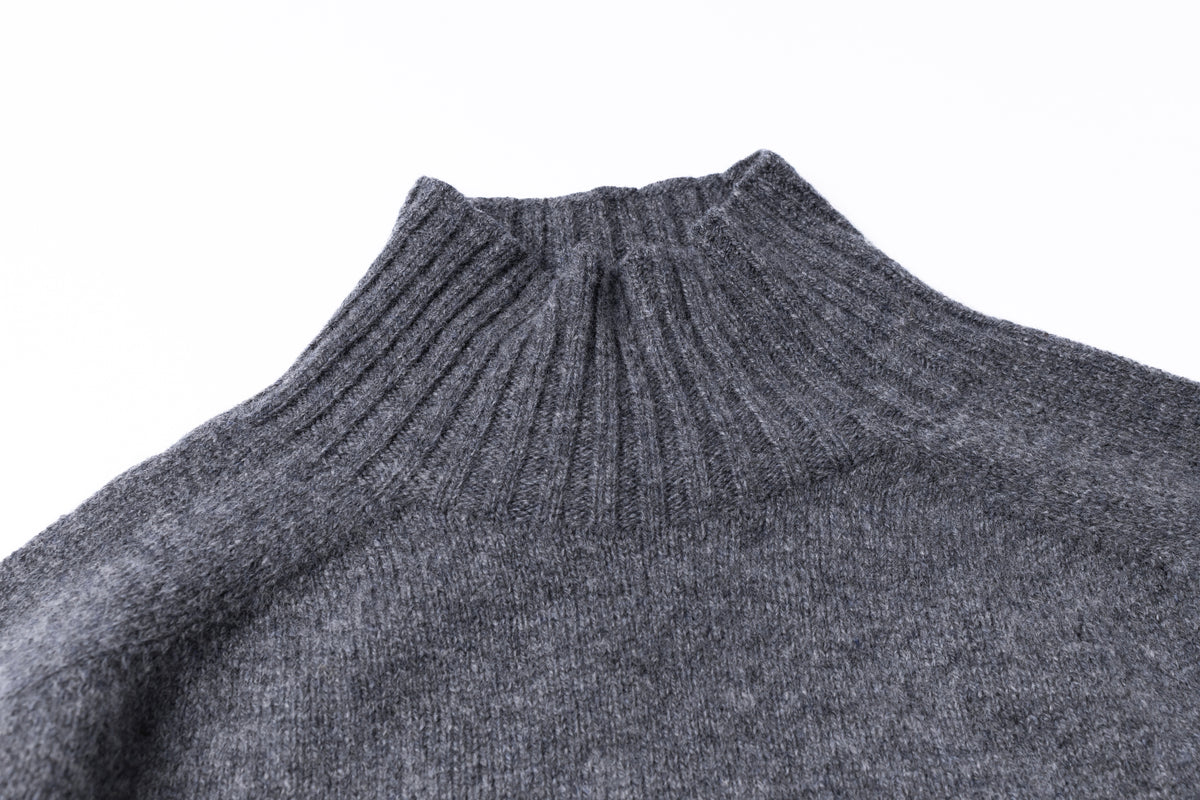 Close-up of a dark gray ribbed knit turtleneck sweater against a plain white background.