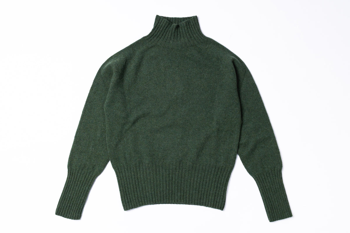 A dark forest green knit turtleneck sweater with long sleeves and ribbed cuffs and hem, laid flat against a white background.