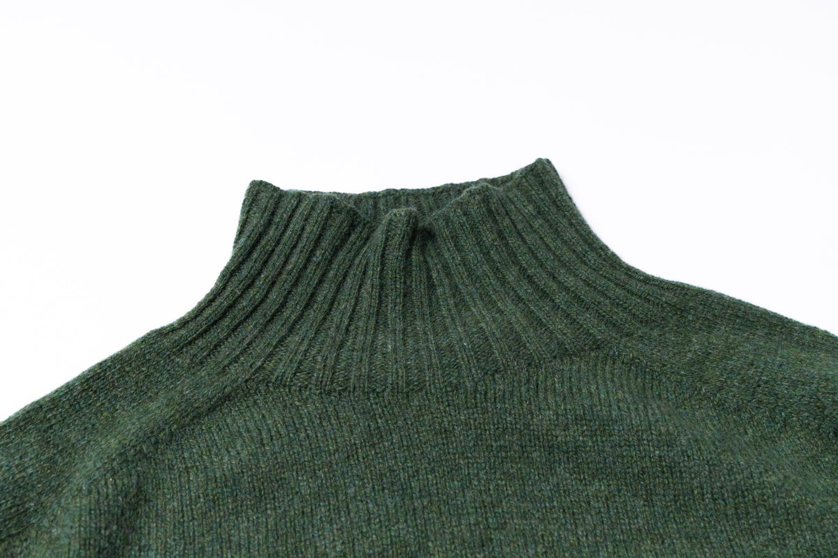 Close-up of a dark green ribbed knit turtleneck sweater on a plain white background.