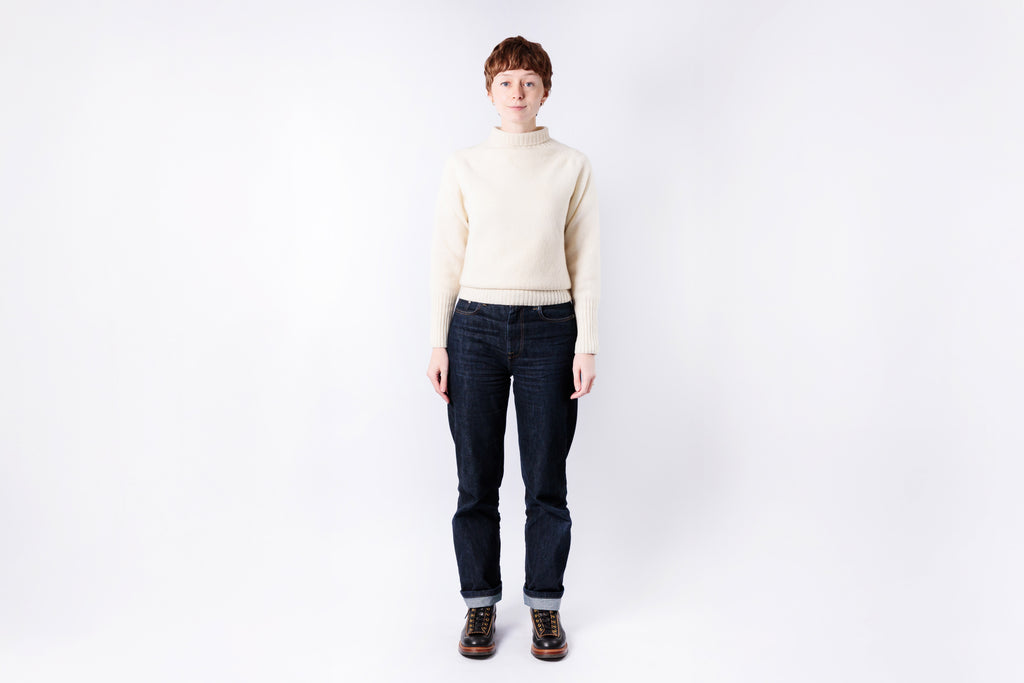 Person wearing a cream sweater and dark jeans on a white background