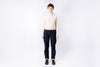 Person wearing a cream sweater and dark jeans on a white background