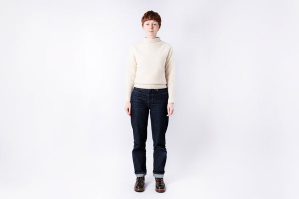 Person wearing a cream sweater and dark jeans on a white background