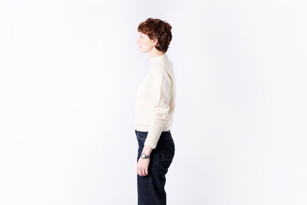 Person wearing a light-colored sweater and dark pants on a white background