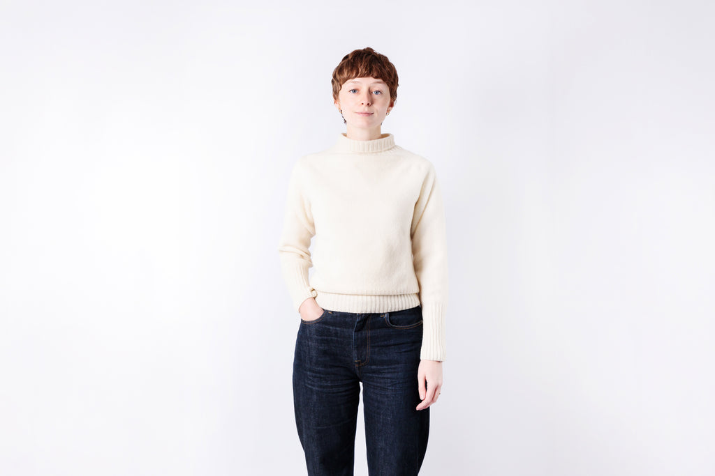 Person wearing a cream sweater and dark jeans against a white background
