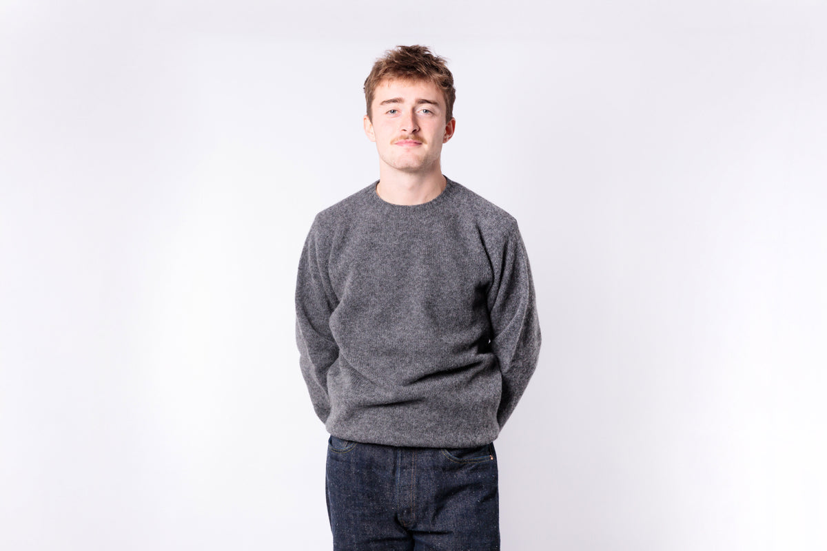 Person wearing a gray sweater and dark jeans on a white background
