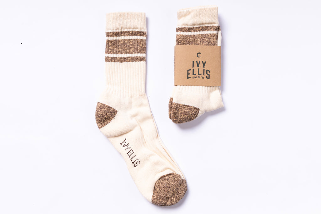 Pair of cream socks with brown accents and a matching cardboard packaging on a white background