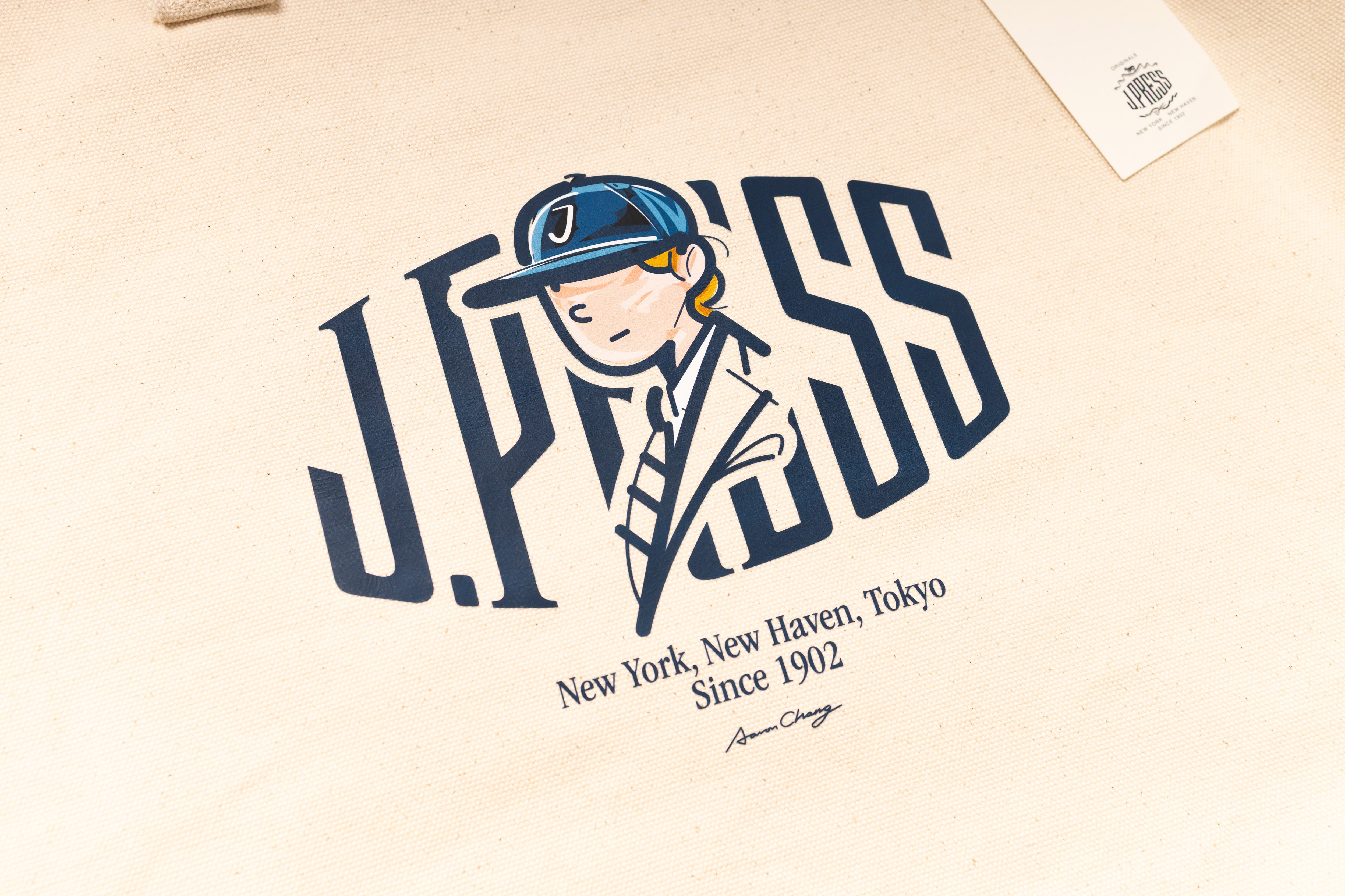 Beige tote bag with a graphic of a person wearing a cap and the text 'J.PRESS' on a beige background.