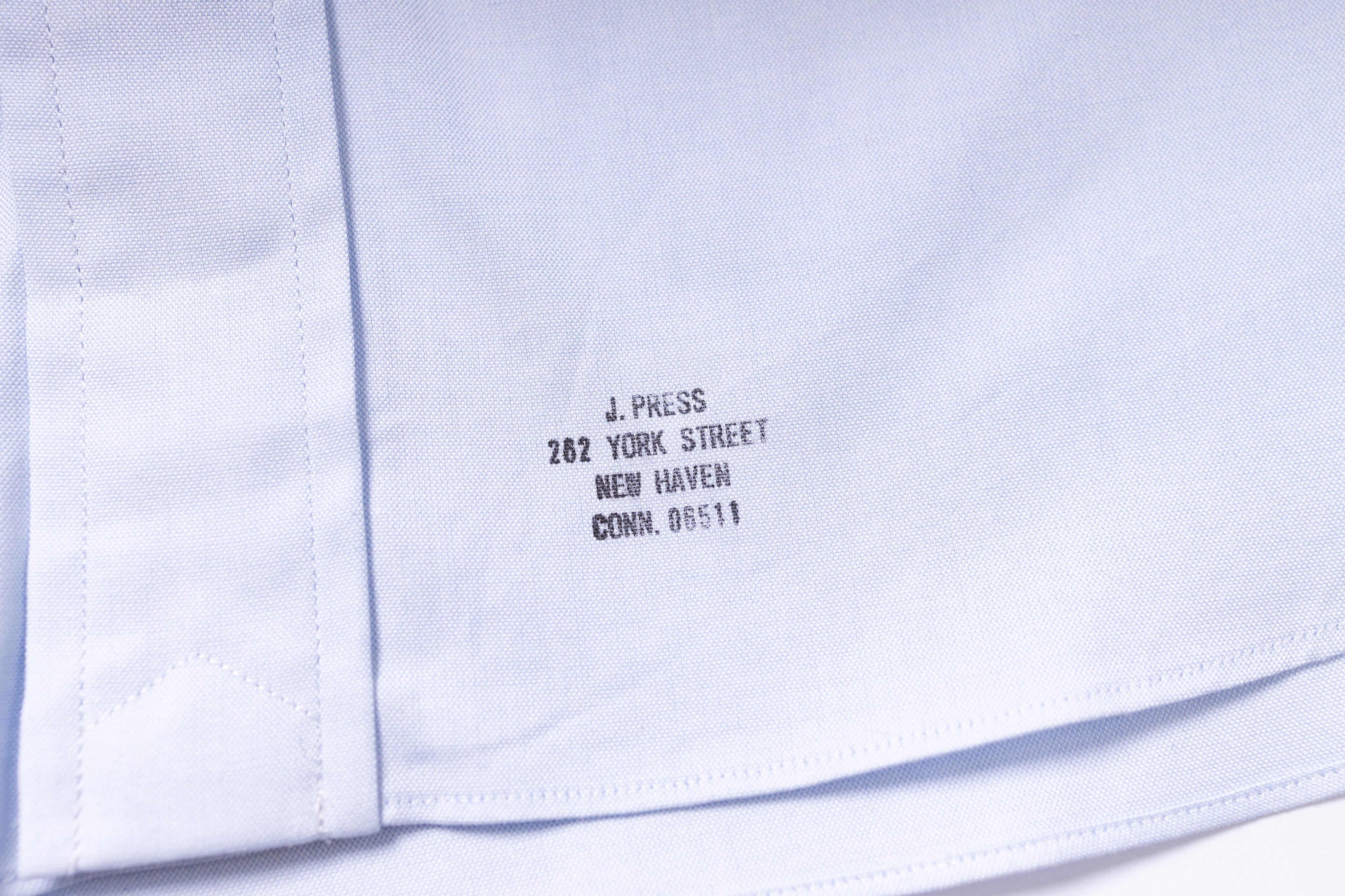 Close-up of a white shirt with black text on the collar, showing 'J. Press' and address details.