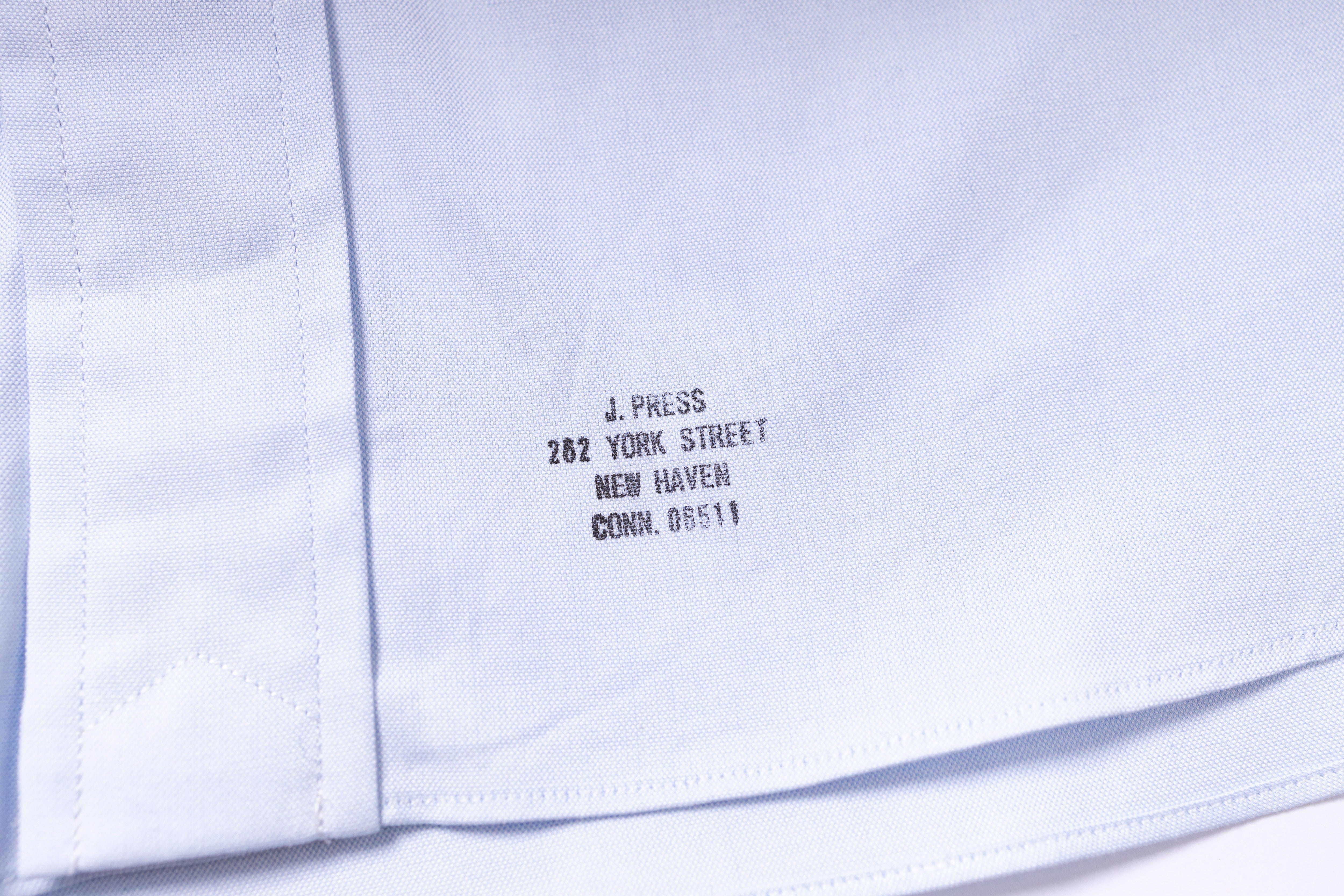 Close-up of a white shirt with black text on the collar, showing 'J. Press' and address details.