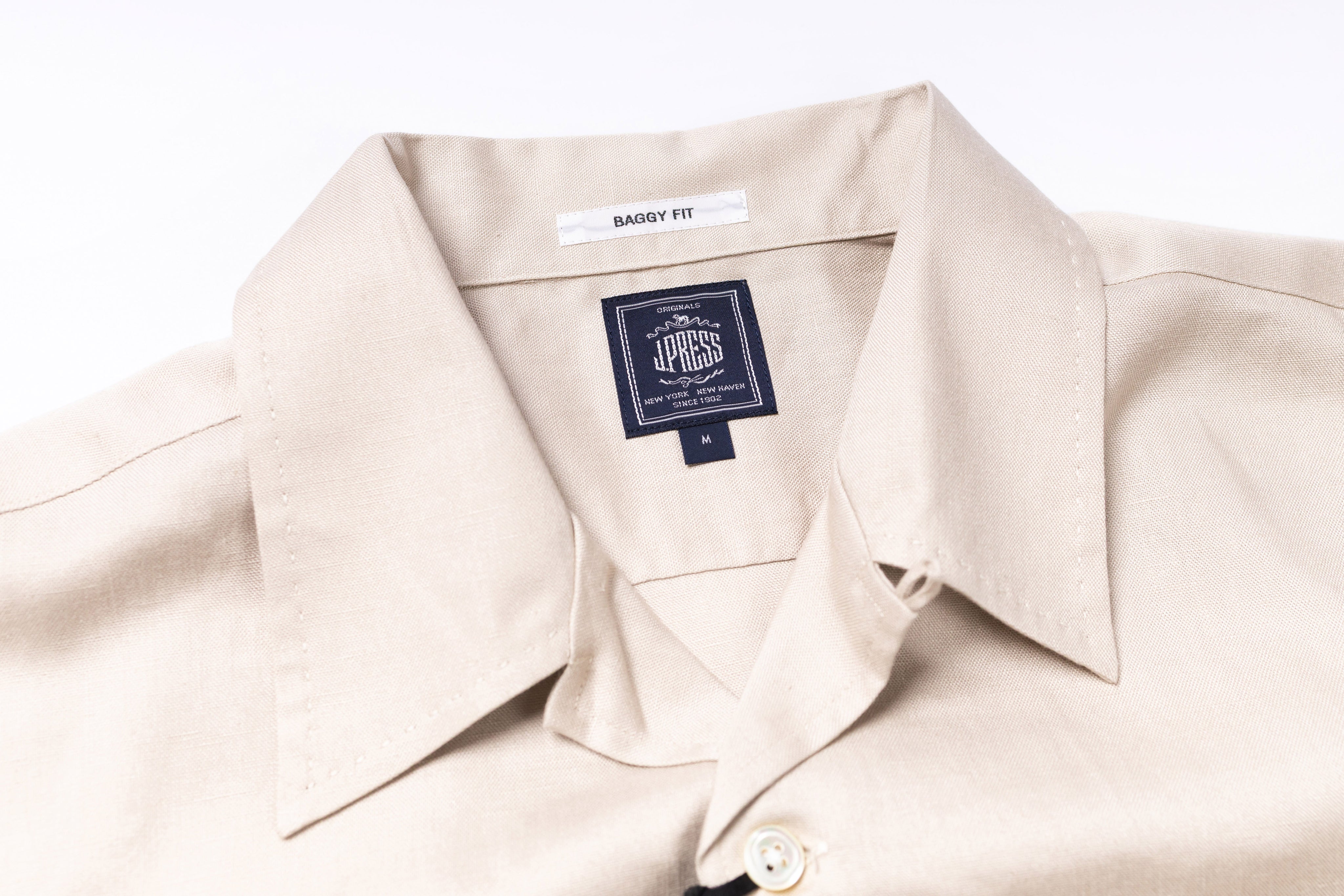 Close-up of a beige shirt with a brand label on a white background