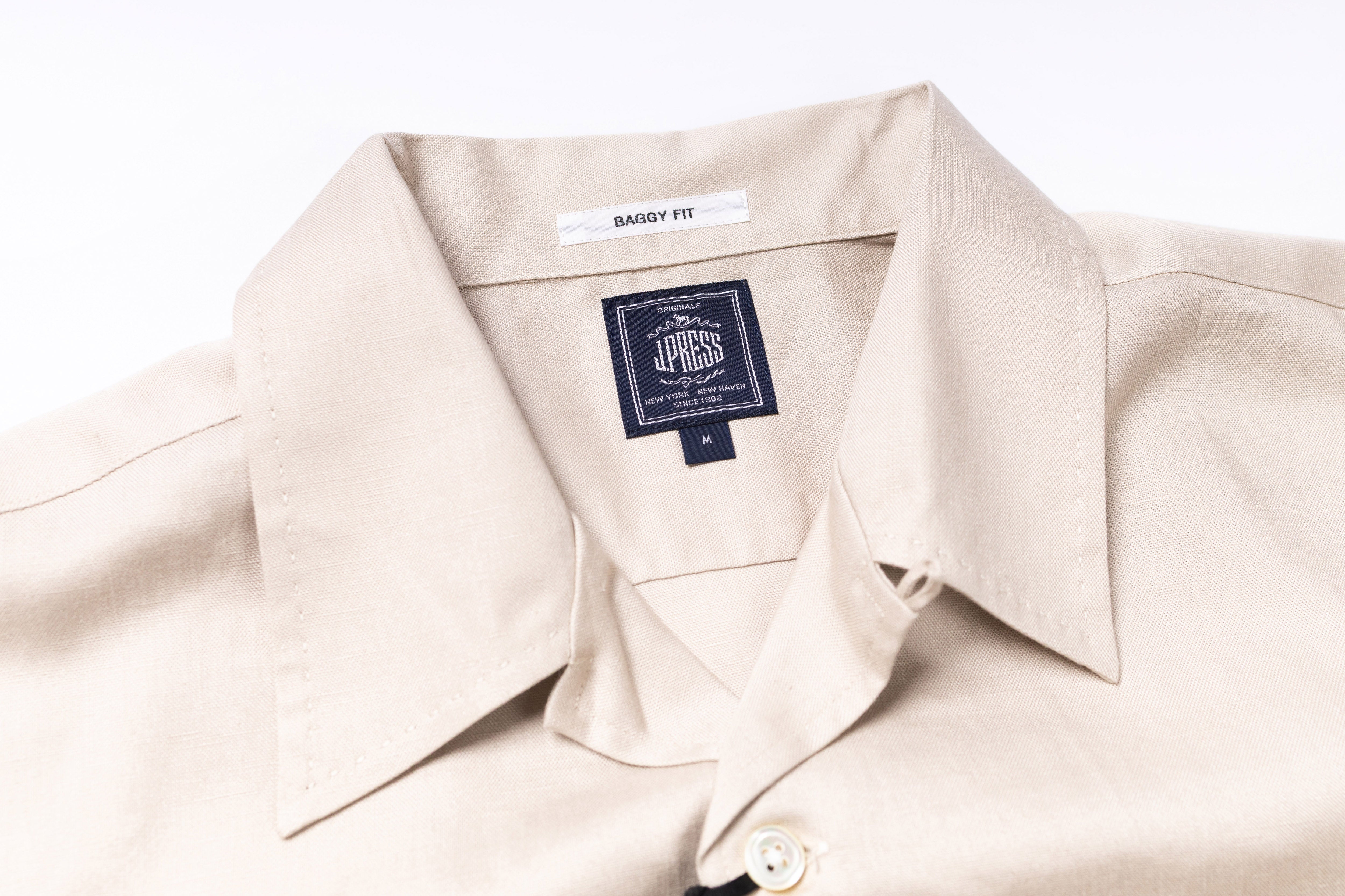 Close-up of a beige shirt with a brand label on a white background