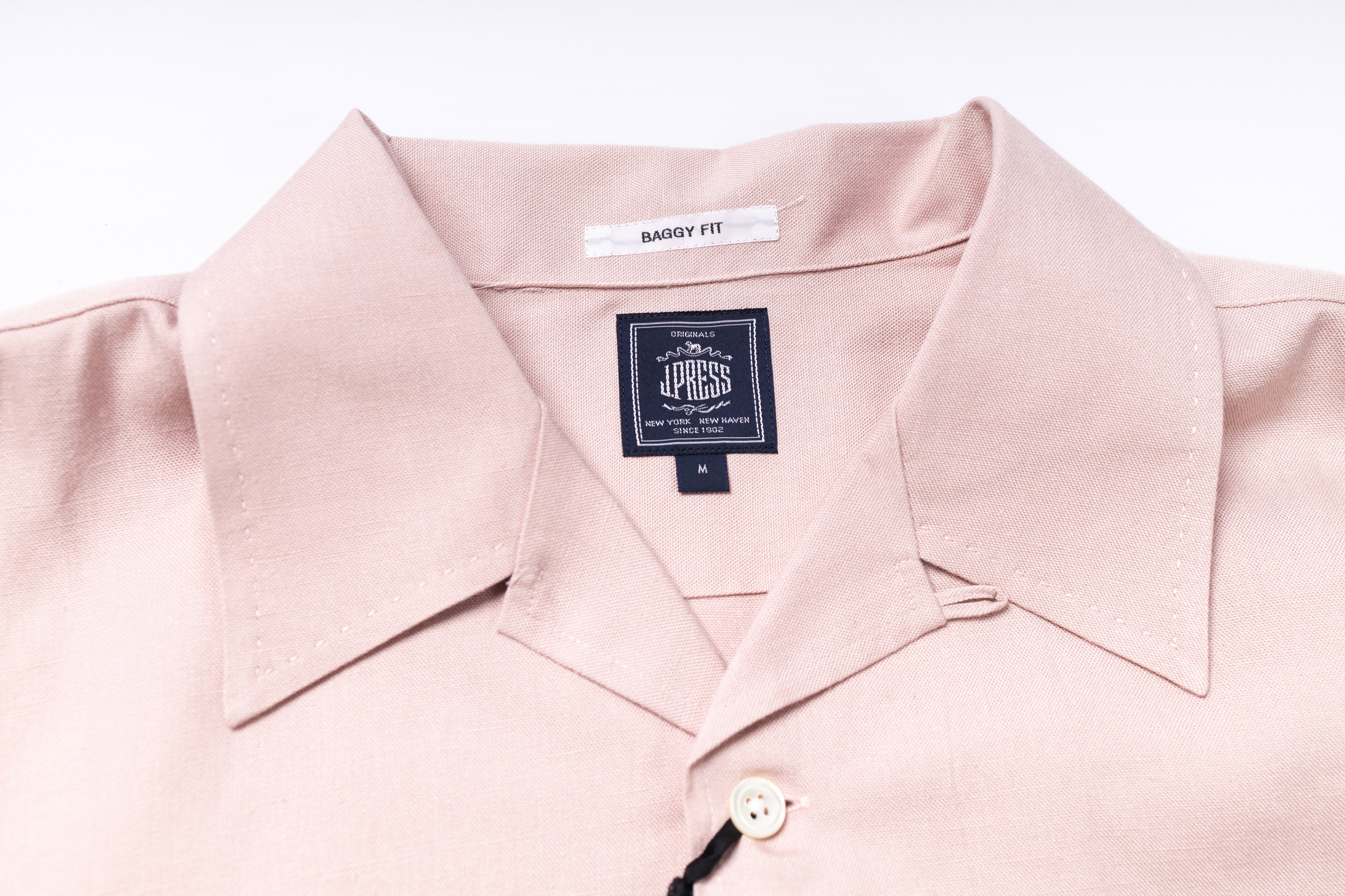Close-up of a light pink shirt with a brand label on a white background