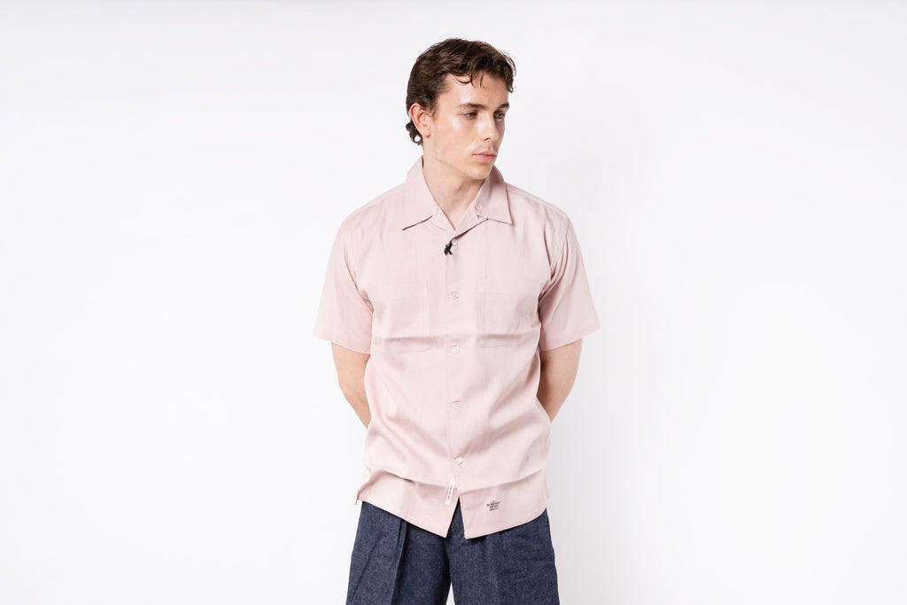 Person wearing a light pink shirt and dark pants on a white background