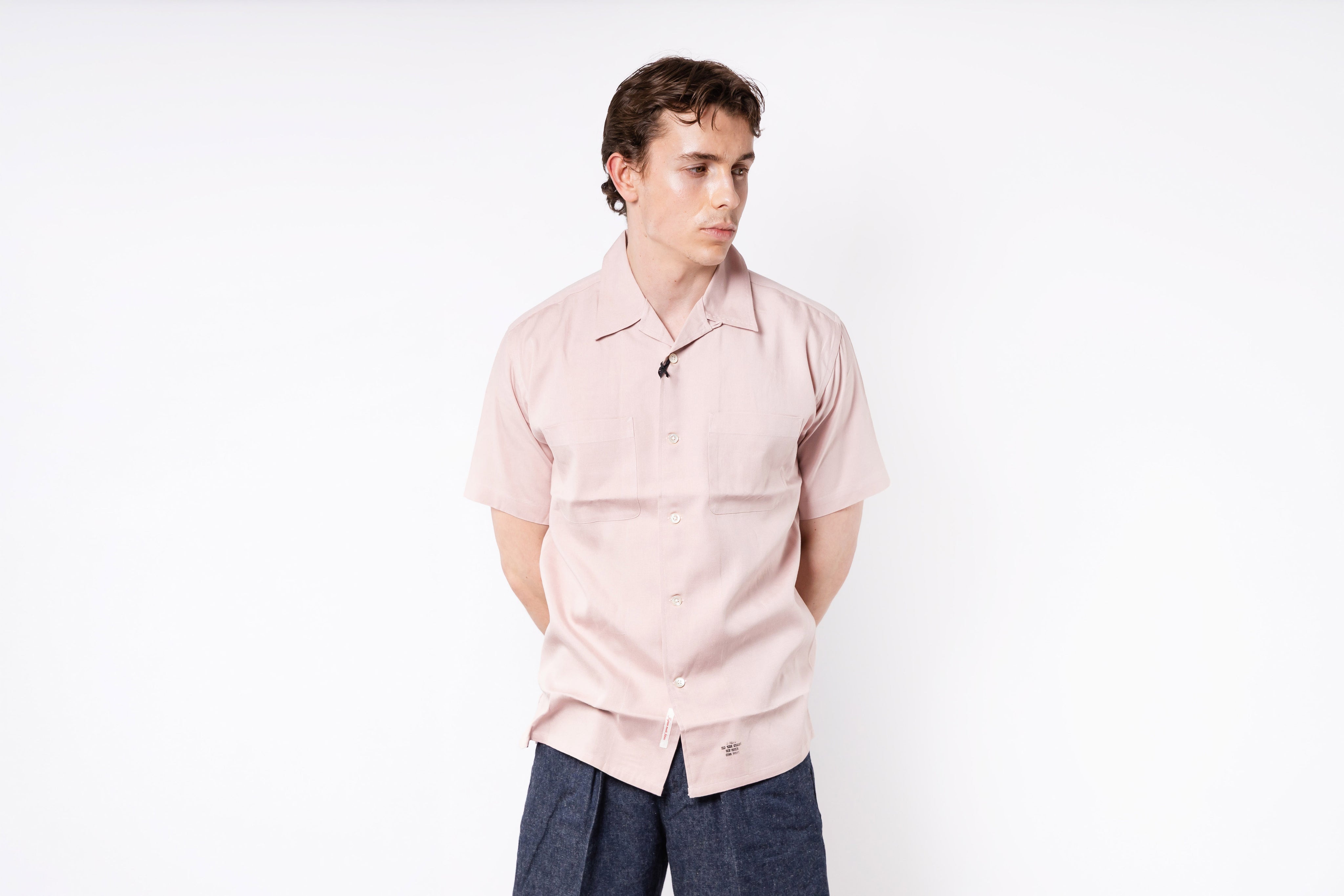 Person wearing a light pink shirt and dark pants on a white background