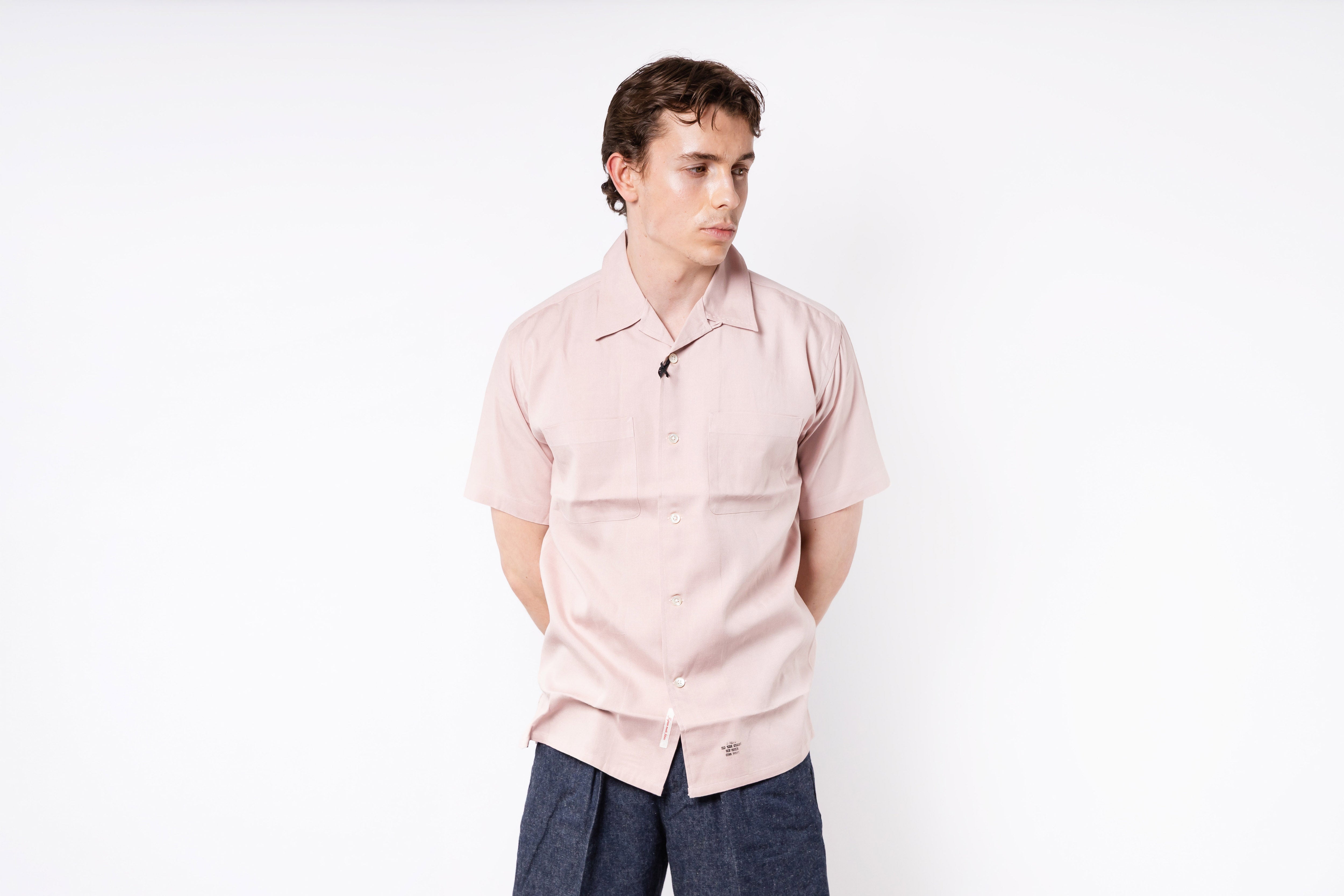 Person wearing a light pink shirt and dark pants on a white background