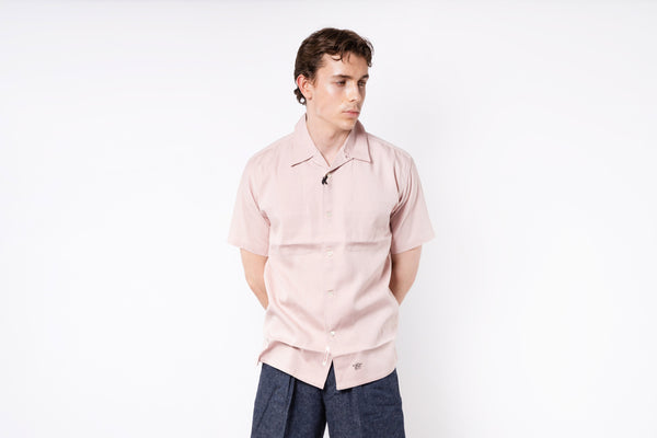 Person wearing a light pink shirt and dark pants on a white background