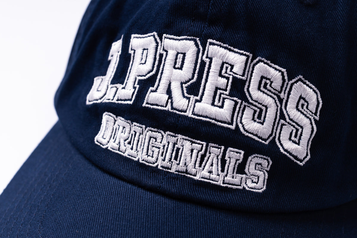 Close-up of a navy blue baseball cap with white embroidered text reading 'J.PRESS ORIGINALS' on the front panel.