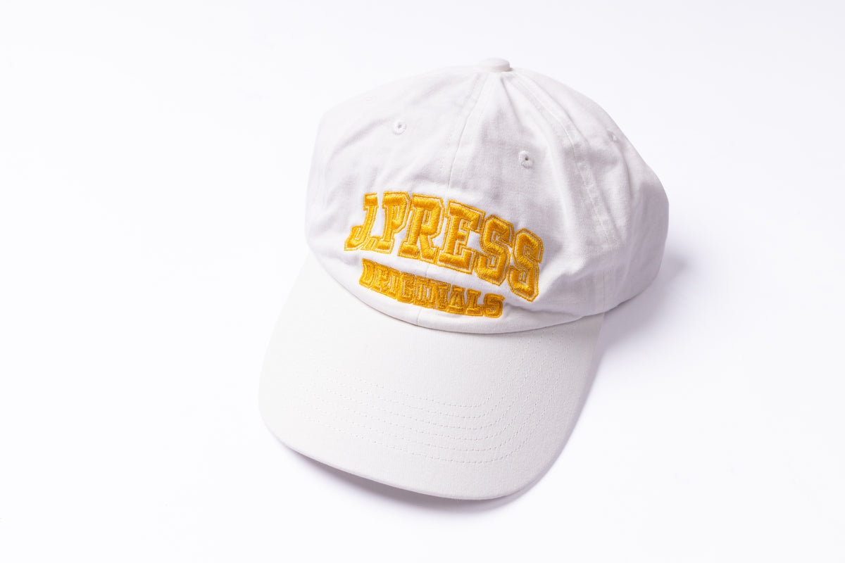 A white baseball cap with yellow embroidered text reading 'PRESS ORIGINALS' on the front, photographed on a clean white background.