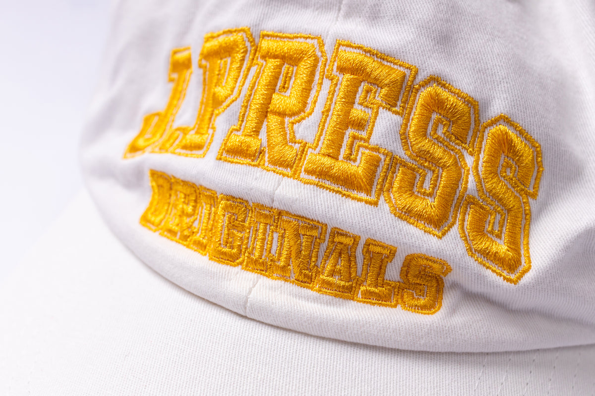 Close-up of a white baseball cap featuring bold yellow embroidered collegiate-style lettering that reads 'PRESS ORIGINALS' on the front panel.