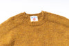 Close-up of a mustard yellow sweater with a brand label on a white background